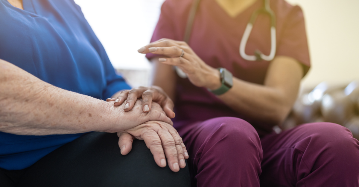 A nurse comforting an older patient holding hands