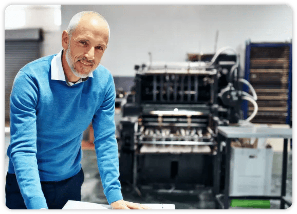 older man in blue shirt standing in front of paper folding machine